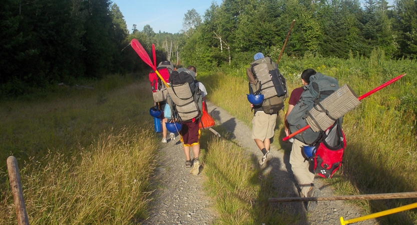 A group of people carry canoe gear along a grassy trail 